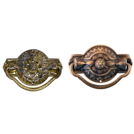 Two brass drawer pulls with ornate detailing, one in a brass finish and the other in an antique brass finish, both featuring a rounded shape and stamped back plates.