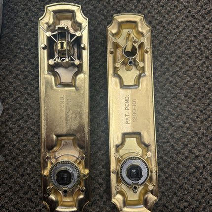 Two brass door handles on a textured black background. Back side picture of escutcheons
