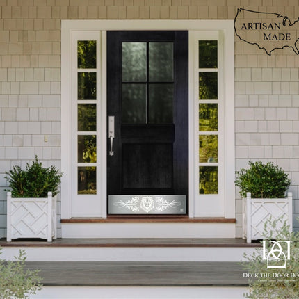 Front door with decorative glass panels  and silver kick plate with lion engraved and planters on a house exterior, featuring 'Artisan Made' and 'Deck the Door Decor' logos.